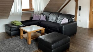 A modern loft-style living room with a black leather sofa, a wooden coffee table, and a grey rug.