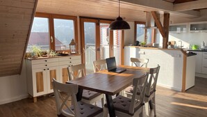 A cozy kitchen with wooden cabinets, a dining table with chairs, and a view of the city through large windows.