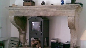 A stone fireplace with a built-in wood stove, a small shelf above it, and a white chair in front.