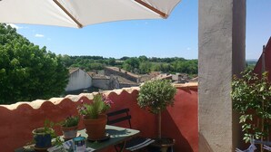 A rooftop terrace with a table, chairs, potted plants, and a view of the surrounding buildings and greenery.