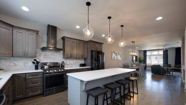 Una cocina moderna con armarios de madera oscura, una isla grande con taburetes de bar, electrodomésticos de acero inoxidable e iluminación colgante.