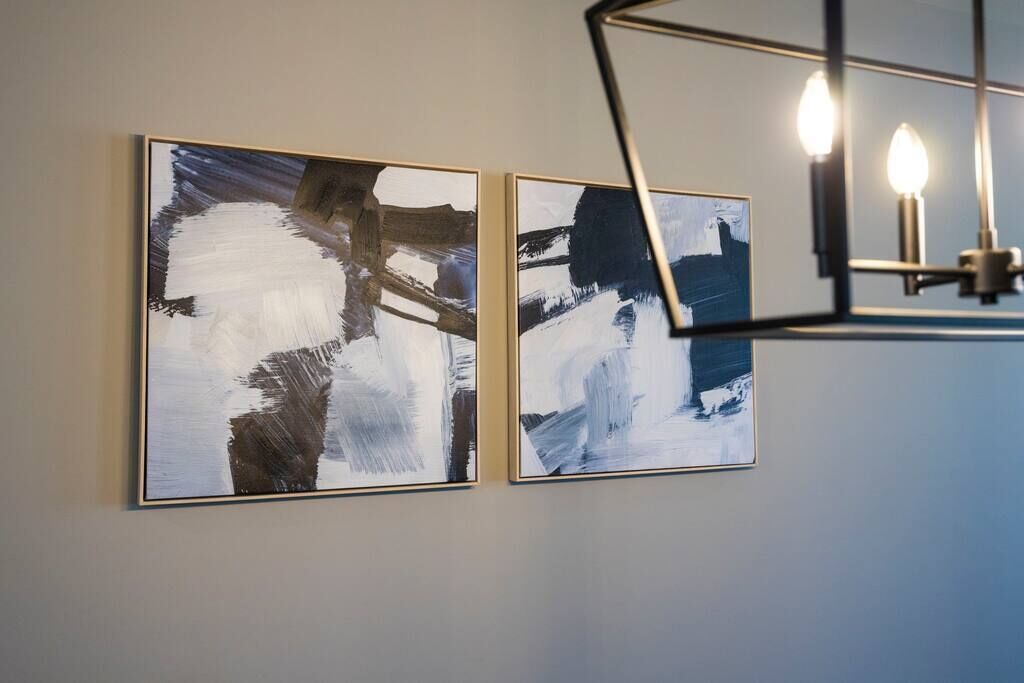 Two abstract paintings on a wall with a modern light fixture above them.
