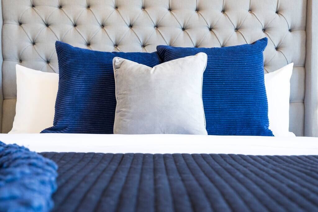 A bed with a tufted headboard, two blue pillows, and a white pillow.