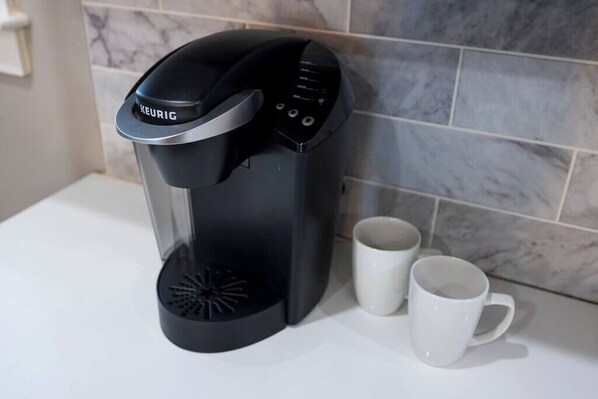 Eine Keurig-Kaffeemaschine steht auf einer weißen Arbeitsplatte, daneben zwei weiße Tassen.