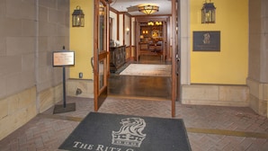 Un'hall d'albergo con un tappetino d'ingresso con su scritto "The Ritz-Carlton" e un cartello che recita "Non portare gli scarponi da sci in hall".