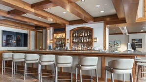 Zona bar con travi in legno, bancone e diversi sgabelli da bar.