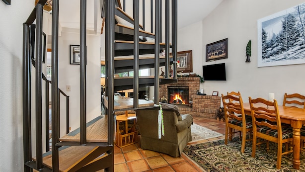 Ein Wohnzimmer mit Kamin, einem Esstisch mit Stühlen, einer Couch und einer Treppe mit Geländer.