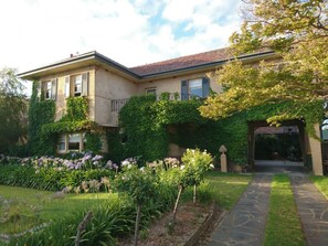 A two-story house with a stone pathway leading to the entrance, surrounded by lush gardens and climbing plants. - Beautiful 2 Story Manor Close to Beach and all (Glenelg)