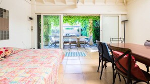 Un dormitori amb un llit, una taula de menjador i cadires, i vista a un pati exterior.