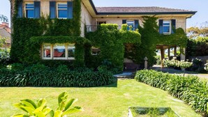 Una casa de dues plantes amb parets cobertes de vitalàcia i un jardí ben cuidat.