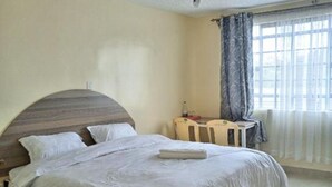 Une chambre à coucher avec un lit, une chaise, une table et une fenêtre avec des rideaux.