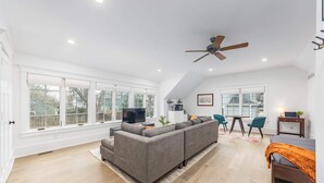 A spacious living room with a large gray sectional sofa, a dining area with a table and chairs, and a ceiling fan. - Tudor Style Carriage House  (Ann Arbor)