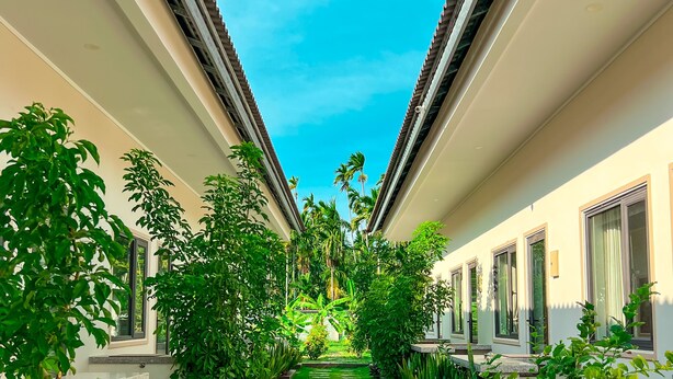 A pathway flanked by lush greenery and a bicycle, leading to a building with a tiled roof and windows. - Areca Muine Homestay (Mui Ne)