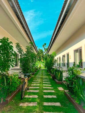 A pathway flanked by lush greenery and a bicycle, leading to a building with a tiled roof and windows. - Areca Muine Homestay (Mui Ne)