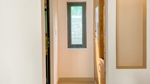 A hallway with a small window, a door, and a light fixture on the wall. - Areca Muine Homestay (Mui Ne)
