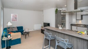 A modern kitchen with a bar area, a blue sofa, and a small dining table. - Cosy Modern Flat - Pass the Keys (Edinburgh)