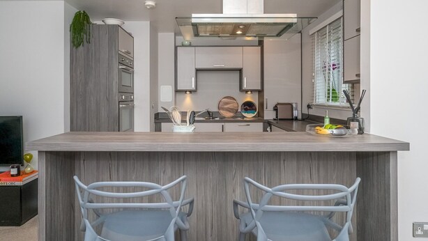 A modern kitchen with a central island, two bar stools, and a built-in oven. - Cosy Modern Flat - Pass the Keys (Edinburgh)