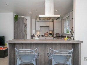A modern kitchen with a central island, two bar stools, and a built-in oven. - Cosy Modern Flat - Pass the Keys (Edinburgh)