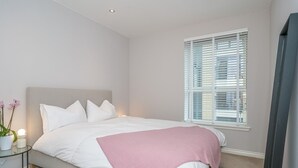 A bedroom with a bed, a bedside table with a lamp, and a window with blinds. - Cosy Modern Flat - Pass the Keys (Edinburgh)