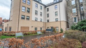 A multi-story residential building with a courtyard featuring benches and leafless shrubs. - Cosy Modern Flat - Pass the Keys (Edinburgh)