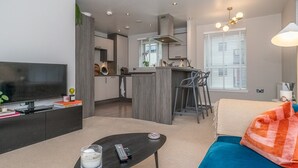 A modern living room with a TV, a coffee table, and a sofa. There is a kitchen area with a dining table and chairs. - Cosy Modern Flat - Pass the Keys (Edinburgh)