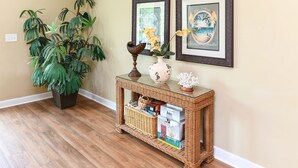 A wicker console table with a vase and a bowl, a potted plant, and framed artwork on a wall. - 5 BR Beach House in Surfside Beach with Private Pool! C-Batical (Surfside Beach)