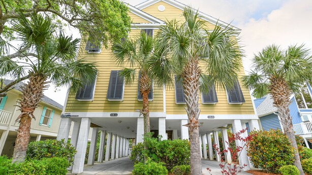 A yellow building with a covered entrance and palm trees in front. - 5 BR Beach House in Surfside Beach with Private Pool! C-Batical (Surfside Beach)