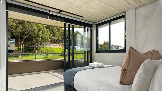 A modern bedroom with a large bed, a view of greenery and buildings outside, and a balcony with glass doors. - Designer Apartment at the Peak of Bo-Kaap | Pool (Cape Town)