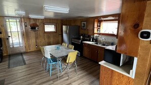 A compact kitchen with wooden cabinets, a dining table with chairs, and a refrigerator. - Cottage on Akers Pond (Errol)
