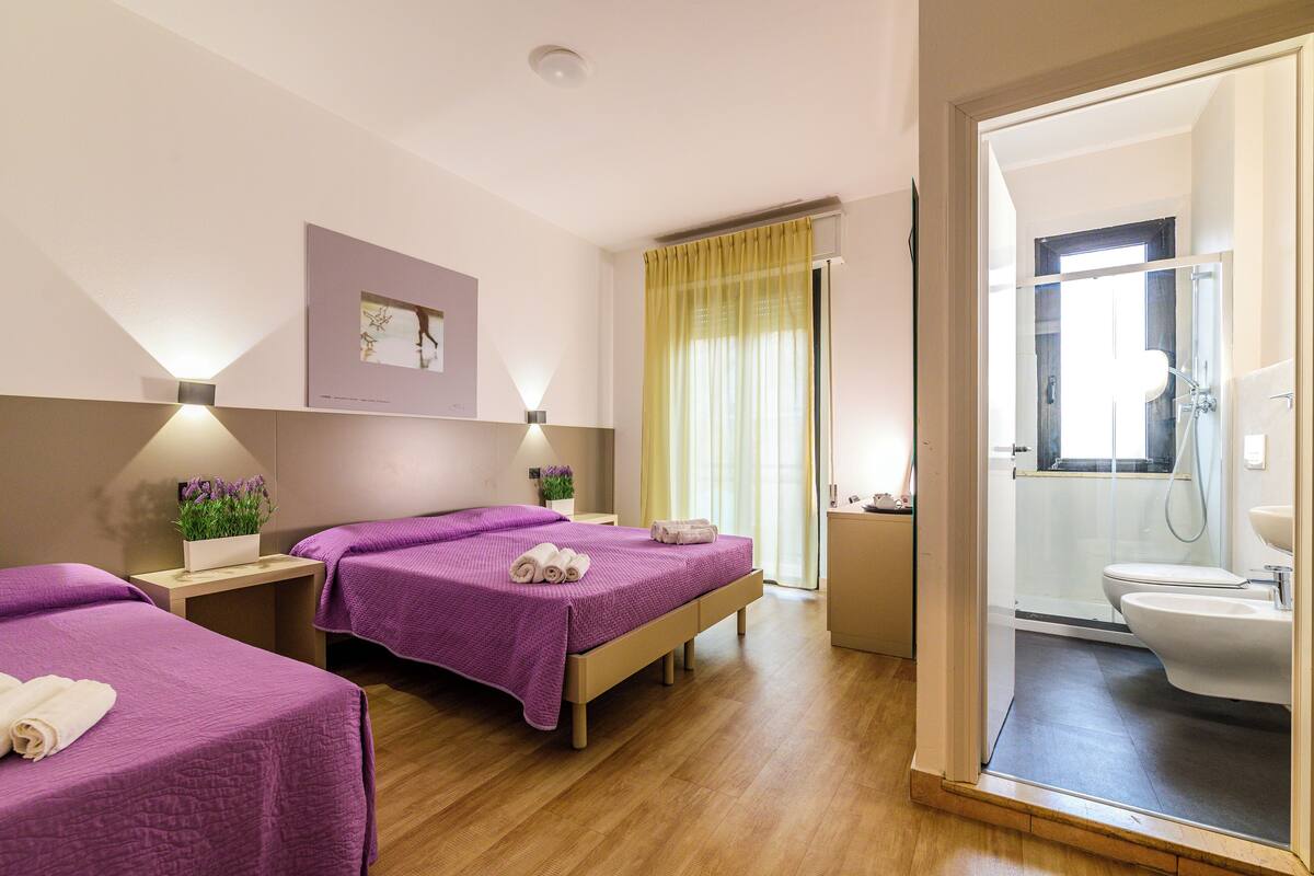 Habitación de hotel con dos camas, baño y zona de ducha.