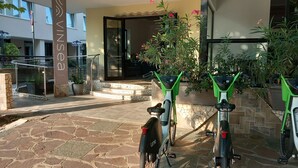 A hotel entrance with a stone-paved patio, a glass railing, and two electric scooters. - Vinsea Hotel (Bellaria-Igea Marina)