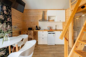 Une cuisine compacte avec des murs en bois, des armoires blanches, une cuisinière encastrée et un petit lave-vaisselle.