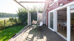 Une terrasse en bois avec une table et des chaises, un barbecue et une vue sur un lac.