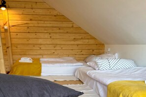 Une pièce avec un plafond en pente, des murs en bois, un lit avec une literie blanche, un oreiller jaune et une couverture grise.