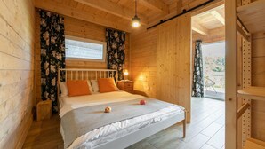 Une chambre à coucher en bois, avec un lit, une table de chevet, une fenêtre avec des rideaux et une porte donnant sur l’extérieur.