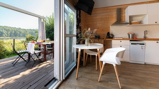 A modern kitchen with a wooden interior, a dining area with a table and chairs, and a view of a lake. - Scandinavian holiday home right by the lake (Klepnica)