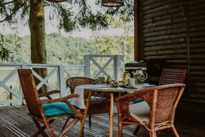 An outdoor dining area with wicker chairs and a table set for two, overlooking a wooded landscape.