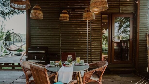 A wooden cabin with a round table and wicker chairs, a grill, and hanging wicker lamps. - Holiday home with a terrace, right by the lake (Klepnica)