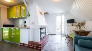 A kitchen with green cabinets, a brick fireplace, and a dining area with a table and chairs. - Holiday home with a terrace, right by the lake (Klepnica)