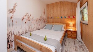 A bedroom with a wooden bed, a nightstand, a lamp, and a window with curtains. - Holiday home with a terrace, right by the lake (Klepnica)