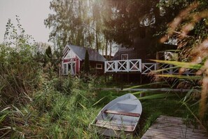A rustic house with a small porch, surrounded by tall grass and trees. - Holiday home right on the lake, terrace (Klepnica)