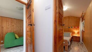 Una habitación con paneles de madera, una cama, un sofá verde y una pequeña mesa con una lámpara.