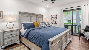 A bedroom with a bed, nightstands, a ceiling fan, a window with curtains, and a view of greenery outside. - Modern 2BR Townhouse - Near Bike Trails & Golf (Bella Vista)