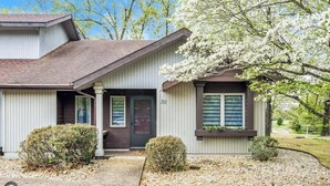 A two-story house with a dark brown roof, white siding, and a number '30' on the front. There are two small bushes in front of the house and a tree with white blossoms to the right. - Modern 2BR Townhouse - Near Bike Trails & Golf (Bella Vista)