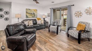 A living room with a leather sofa, two armchairs, a ceiling fan, and a large abstract painting. - Modern 2BR Townhouse - Near Bike Trails & Golf (Bella Vista)