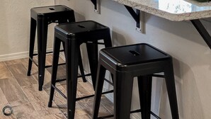 A kitchen with a white countertop, three black stools, and a wooden floor. - Modern 2BR Townhouse - Near Bike Trails & Golf (Bella Vista)