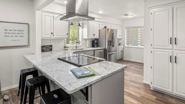 A modern kitchen with white cabinetry, a central island with stools, and a large refrigerator. - Modern 2BR Townhouse - Near Bike Trails & Golf (Bella Vista)
