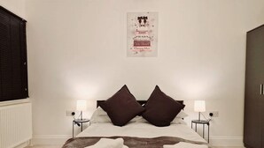A neatly made bed with two pillows, two bedside tables with lamps, and a poster on the wall. - Deluxe 2 Bed Apartment in Uxbridge (Uxbridge)