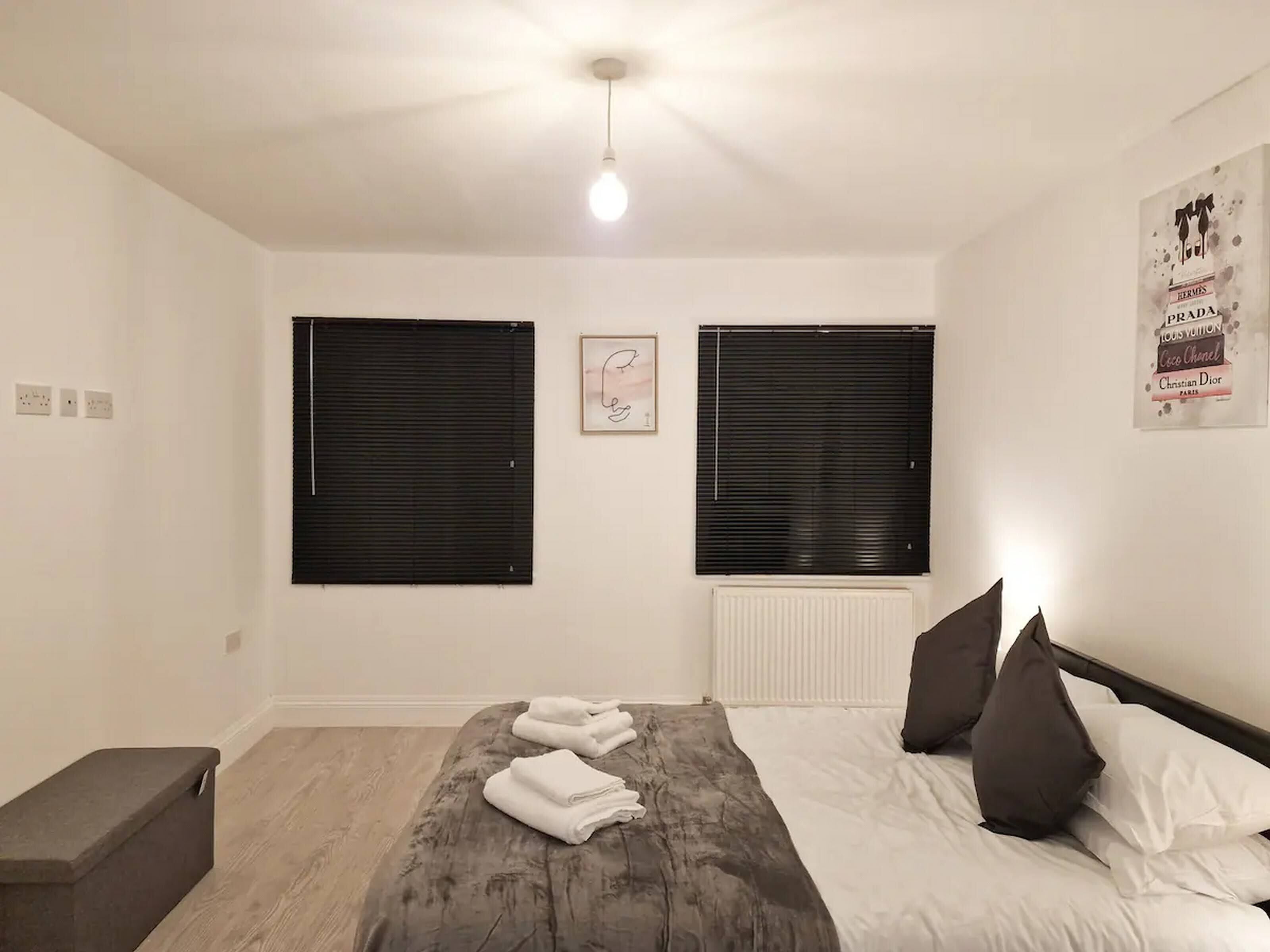 Une chambre à coucher avec un lit, deux fenêtres, un radiateur et un luminaire.