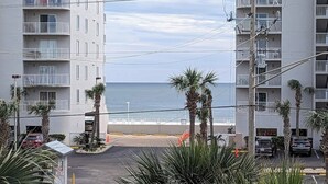 Ein Strandhotel mit mehreren Balkonen, einem Parkplatz und Palmen.